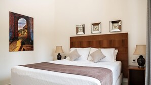A neatly made bed with a wooden headboard, two bedside tables with lamps, and a framed picture on the wall. - Elegant Chania Villa for 4 Guests (Kissamos)