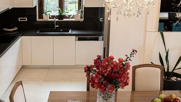 A modern kitchen with white cabinets, a dining table with chairs, a chandelier, and a vase with flowers. - Elegant Chania Villa for 4 Guests (Kissamos)