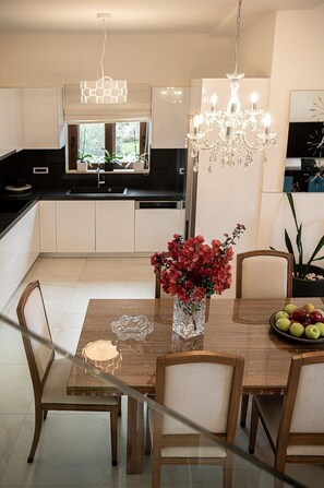 Una cucina moderna con mobili bianchi, un tavolo da pranzo con sedie, un lampadario e un vaso con fiori.