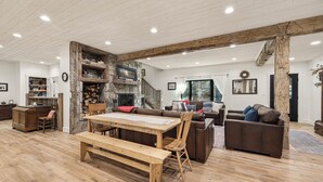 Ein geräumiges Wohnzimmer mit einem Holzessttisch, Bänken, einem Kamin und einer Treppe, die zu einer weiteren Ebene führt.