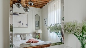 A bedroom with a large mirror, a bed with pillows, a bedside table, and a window with curtains.
