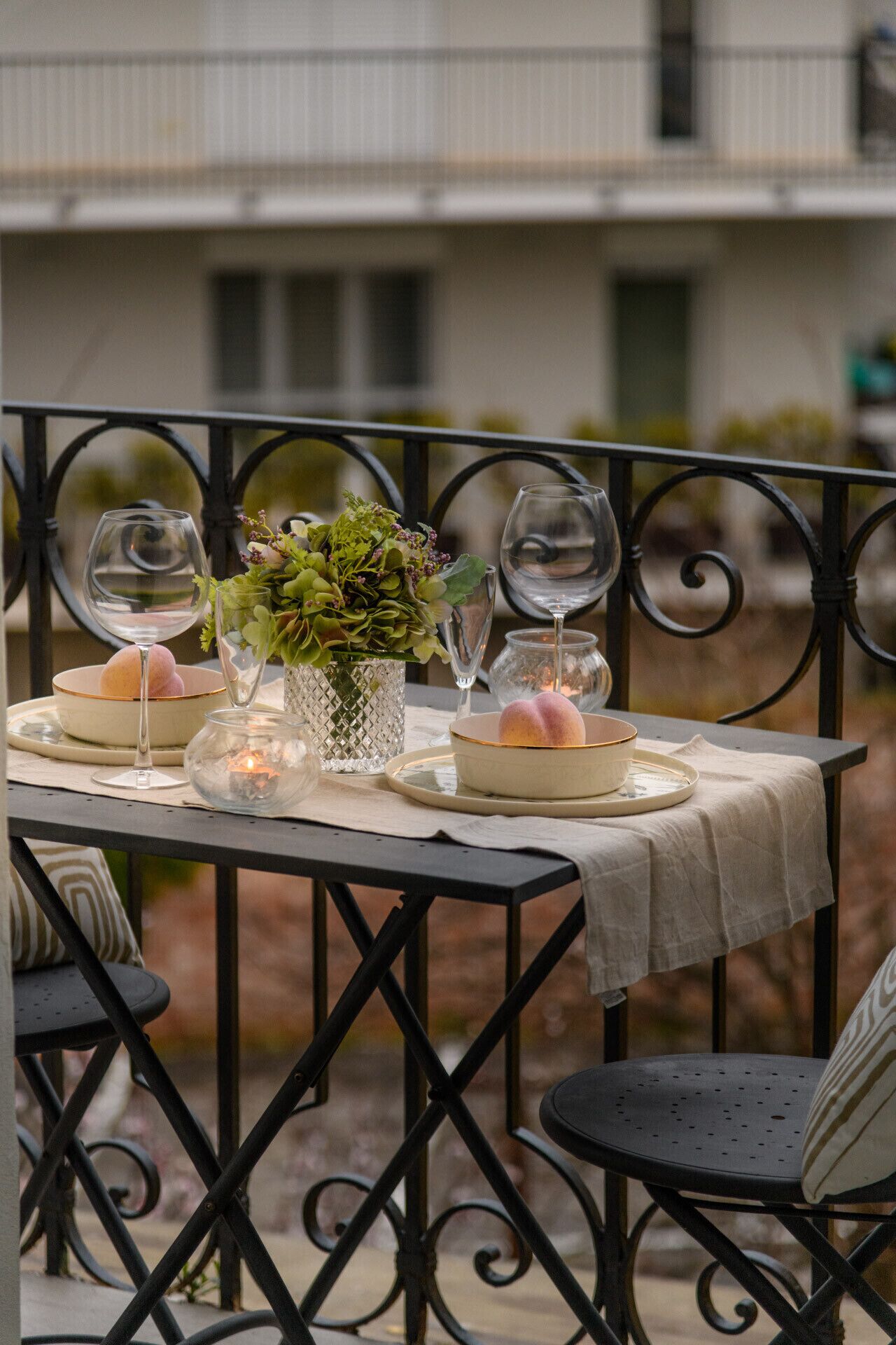 Une table de jardin, dressée pour un repas en plein air, avec des verres à vin, des bols et un vase décoré de verdure.