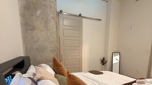 Ein Hotelzimmer mit Bett, digitaler Uhr, Handtuch, Spiegel und Tür.