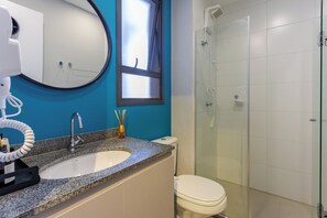 Ein Badezimmer mit Granitwaschtisch, Toilette in Weiß, Duschkabine aus Glas und Spiegel mit runder Umrandung.