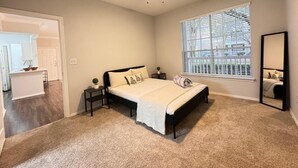 Ein Schlafzimmer mit Bett, Deckenventilator, Fenster mit Jalousien und einer Tür zu einem Badezimmer.