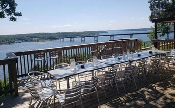 An outdoor dining area with a view of a bridge over water, metal chairs, and a long table. - EAGLES NEST MOTEL & LOUNGE (Lake Ozark)
