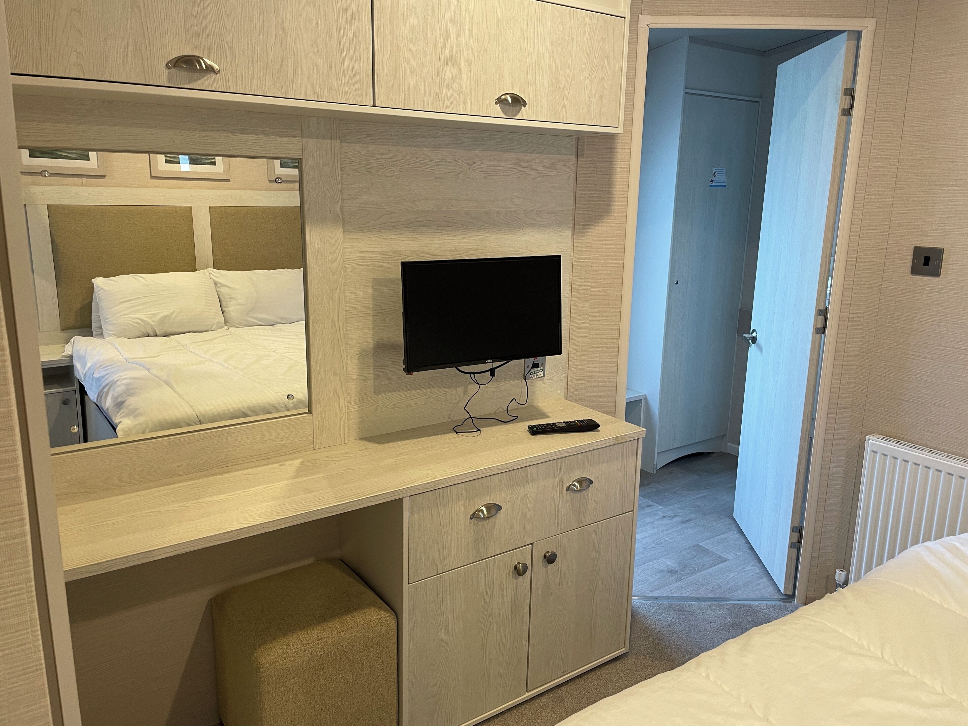 Una habitación de hotel con una cama, televisión, escritorio con cajones y espejo.