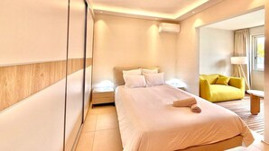 A modern hotel room with a large bed, bedside tables, a yellow armchair, and a small round table. - Nice Deluxe, Premium One-Bedroom Apartment (Saint-Denis)