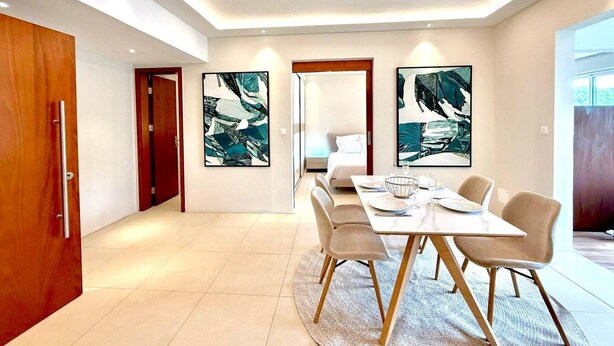 A modern dining area with a table set for four, a wooden door, and abstract art on the walls. - Nice Deluxe, Premium One-Bedroom Apartment (Saint-Denis)