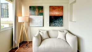 A modern living room with a sofa, two abstract paintings, a floor lamp, and a window with curtains. - Nice Deluxe, Premium One-Bedroom Apartment (Saint-Denis)