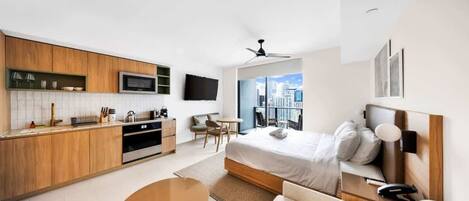 Une chambre d’hôtel moderne dotée d’une kitchenette, d’un lit avec une tête de lit, d’un coin salon et offrant une vue sur la ville.