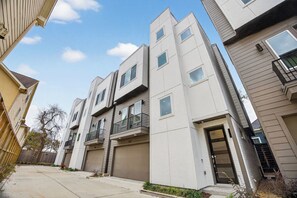 A modern multi-story residential building with balconies, a garage, and a clear sky. - Modern EaDo Stay - 3BR Townhome w/ Private Deck (Houston)