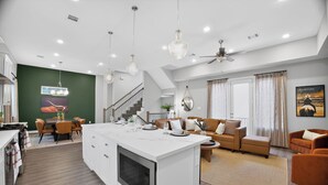 Eine moderne Küche mit Kochinsel, ein Essbereich mit Tisch und Stühlen, ein Wohnzimmer mit Sofa und Couchtisch sowie eine Treppe, die in eine obere Ebene führt.