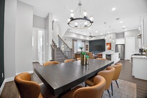 A modern kitchen with white cabinets, a stainless steel refrigerator, and a dining area with a dark wood table and leather chairs. - Modern EaDo Stay - 3BR Townhome w/ Private Deck (Houston)