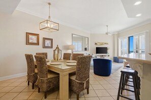 Un coin repas avec une table dressée pour six personnes, entouré de chaises en osier, d’un lustre et de tableaux encadrés accrochés au mur.