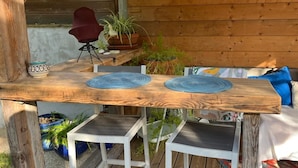 Eine Holzterrasse mit Tisch und zwei Stühlen, umgeben von Topfpflanzen und einer Holzverkleidung.