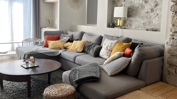 Ein modernes Wohnzimmer mit grauem Sofa, einem runden Couchtisch und einer Wand mit Steinverkleidung.