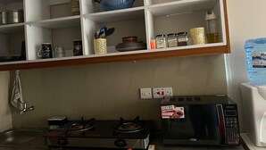 A kitchen with a gas stove, a microwave, and a shelf with various kitchen items. - Snowhaven Kiambu rd| Studio Apt - Swimming pool (Nairobi)