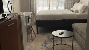 A hotel room with a bed, a desk, a chair, a small round table, a television, and a window with curtains. - Snowhaven Kiambu rd| Studio Apt - Swimming pool (Nairobi)