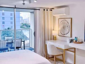 A hotel room with a bed, a desk, a chair, a lamp, and a framed artwork on the wall.