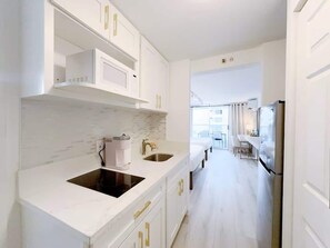 A modern kitchen with white cabinetry, a black sink, and a stainless steel refrigerator.