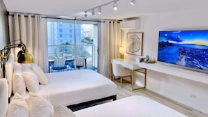 A hotel room with two beds, a desk, a chair, a TV, and a window with a view of buildings. - @ Marbella Lane- Trendy Waikiki Oasis Near Beach (Honolulu)