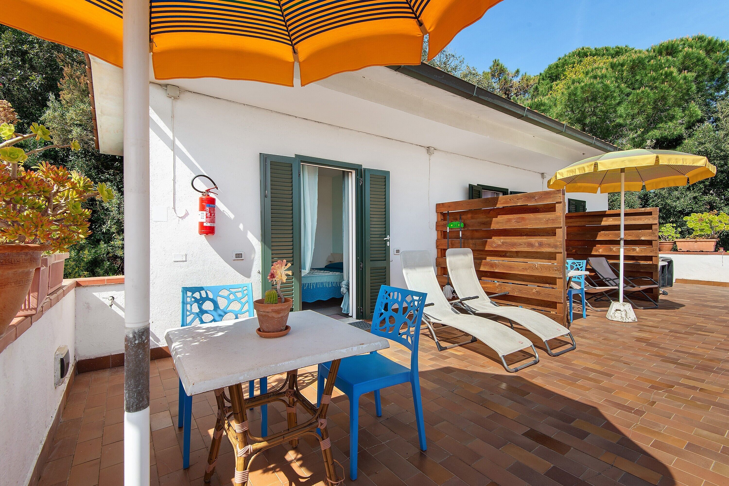 Eine Terrasse mit Tisch und Stühlen, ein Holzboden und ein an der Wand befestigter Feuerlöscher.