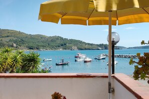 A balcony with a yellow umbrella, overlooking a marina with boats, greenery, and a hilly landscape. - Sciabattica Room 2 with Sea View, Private Terrace, and Wi-Fi (Lacona)