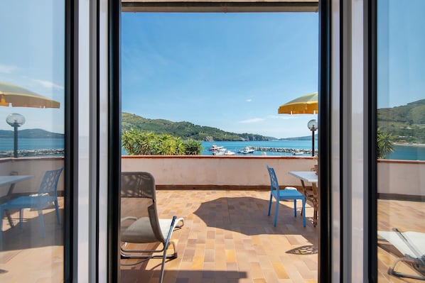 Une terrasse avec vue sur la mer, des chaises, des tables et des parasols.