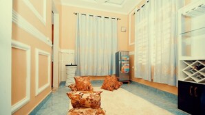 Una habitación con sofá, alfombra, refrigerador y cortinas.