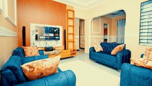 Una sala de estar con sofás azules, un panel de madera en la pared, un televisor y una estantería.
