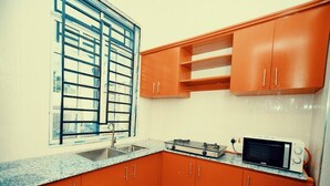 Una cocina funcional con lavamanos, estufa, microondas y armarios color naranja.