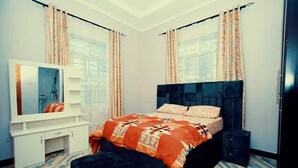 Un dormitorio con cama, cómoda, espejo y cortinas.