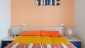 Un lit avec une literie orange, deux lampes de chevet et un luminaire fixé au mur.