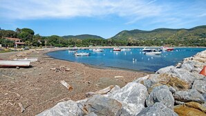 Une zone côtière où des bateaux sont amarrés, avec une rive rocheuse et des collines en arrière-plan.