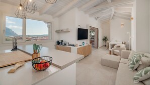 A modern kitchen with a large island, a dining area with a sofa, and a TV in the background. - VILLA CIELO DI TAVOLARA, just a few steps from the sea with breathtaking views. (Porto San Paolo)