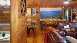 A cozy cabin interior with a dining area, a leather sofa, and a scenic view of mountains. - <10 Min to Lake & DT! Flat Drive! Hot Tub! Games! (Blue Ridge)
