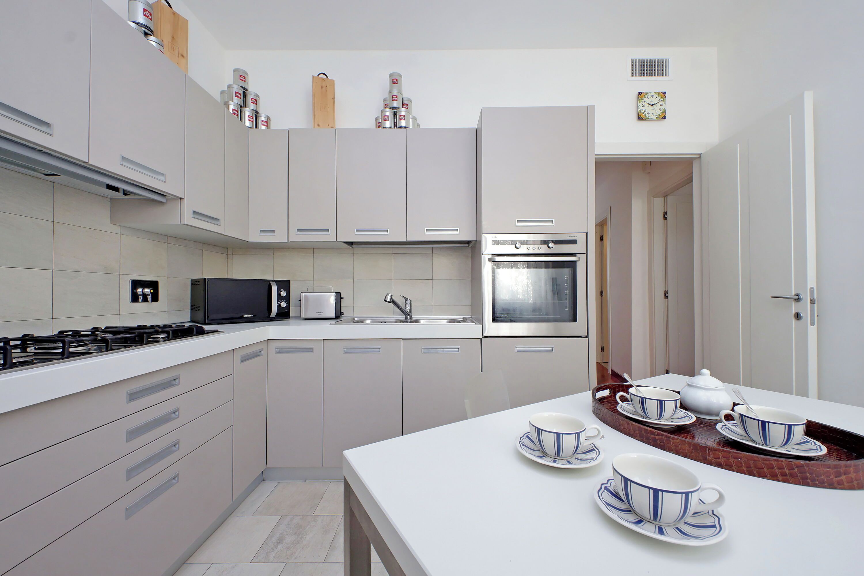 A modern kitchen with white cabinets, a microwave, stove, and an oven. There are tea sets on the counter.