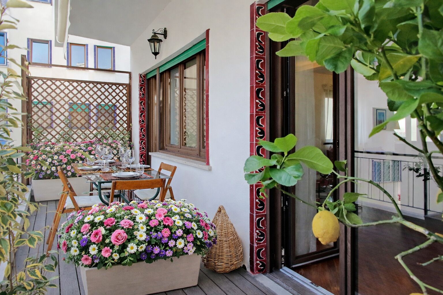 Un balcon avec une table dressée pour le dîner, un panier en osier et un pot de fleurs aux fleurs jaunes.