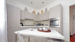 Una cocina moderna con armarios blancos, electrodomésticos de acero inoxidable y una mesa de comedor blanca.