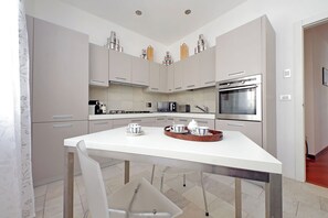 A modern kitchen with white cabinets, stainless steel appliances, and a white dining table. - BELVEDERE RESIDENCE - BALCONY - JACUZZI - Air Conditioning - Wi-Fi - LUXURY (Roma)