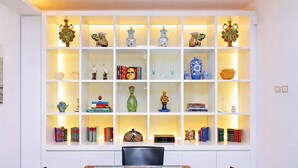 Una habitación con una mesa de comedor de vidrio, estantes blancos con adornos y libros.