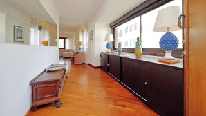 Un pasillo con suelo de madera, un mueble oscuro, una puerta de cristal y una ventana con vistas.