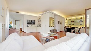 Una sala de estar moderna con un sofá, una mesa de centro y un televisor. Hay una zona de cocina con armarios y una mesa de comedor.