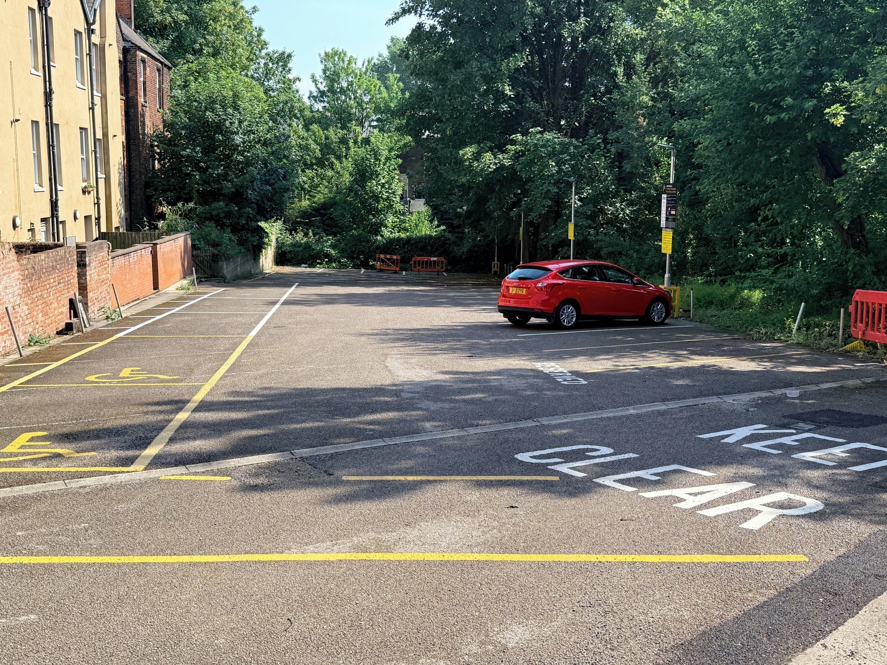 Un estacionamiento con señalización clara para plazas de estacionamiento para discapacitados y un coche rojo aparcado.
