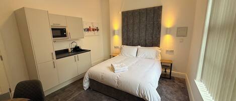 Ein Hotelzimmer mit Bett, Schreibtisch, Mikrowelle, Spüle und einem Fenster mit Jalousien.