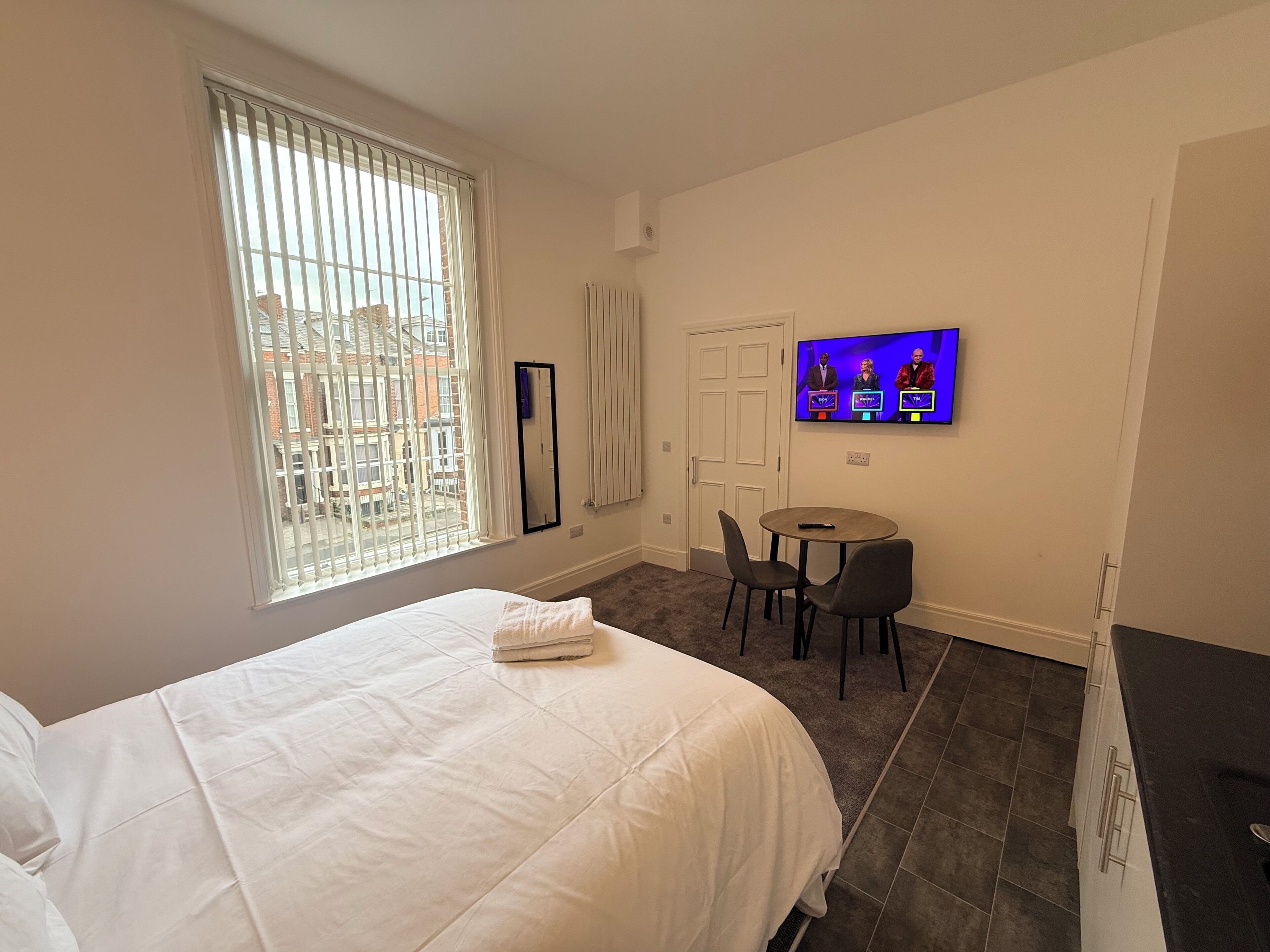 Ein Hotelzimmer mit einem Bett, einem Fernseher, einem kleinen Tisch und einem Fenster mit Jalousien.
