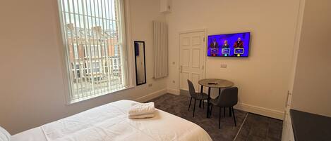 Een hotelkamer met een bed, een televisie, een klein tafeltje en een raam met zonwering.