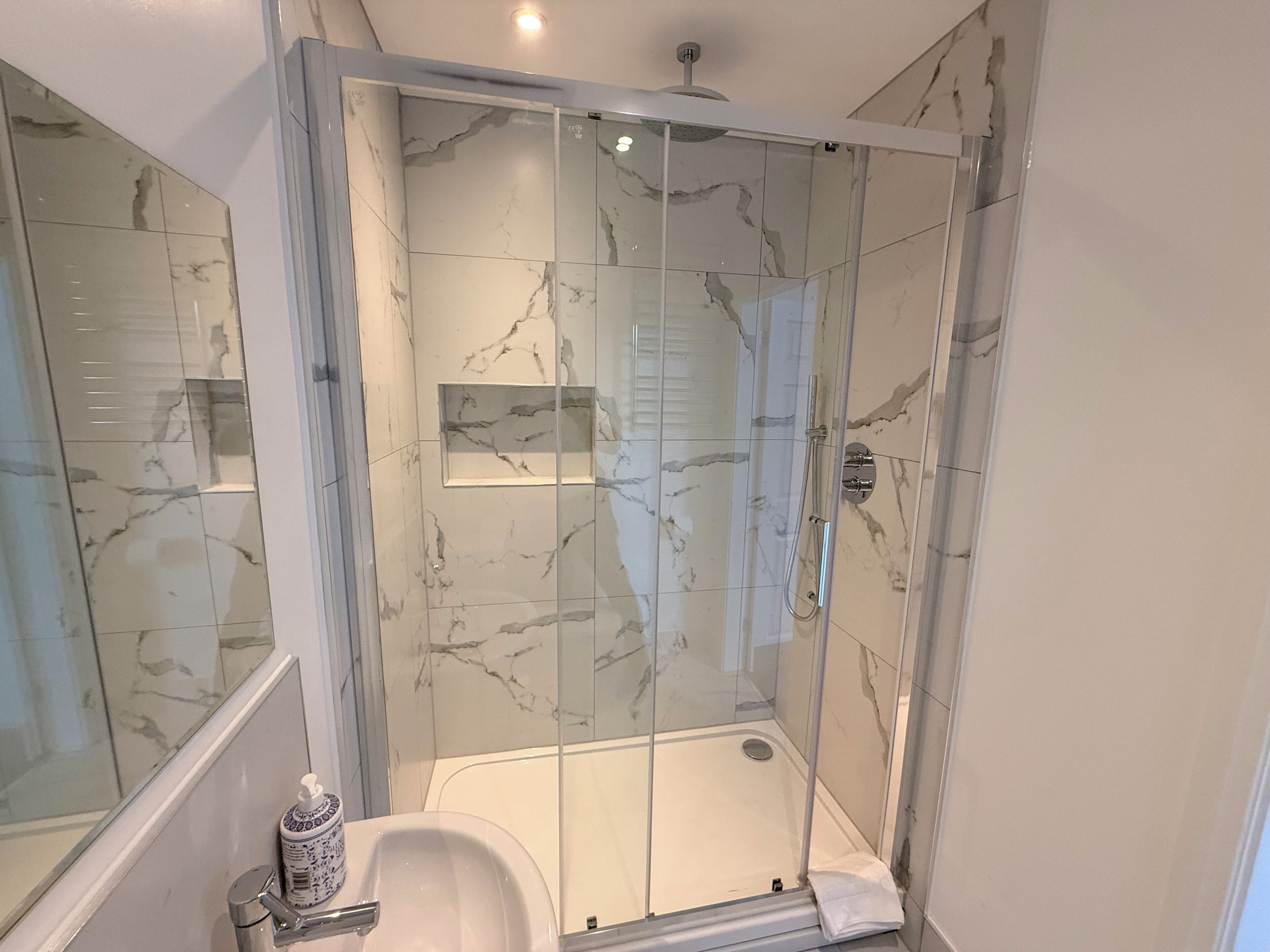 A modern bathroom with a glass-enclosed shower, marble walls, and a white sink.