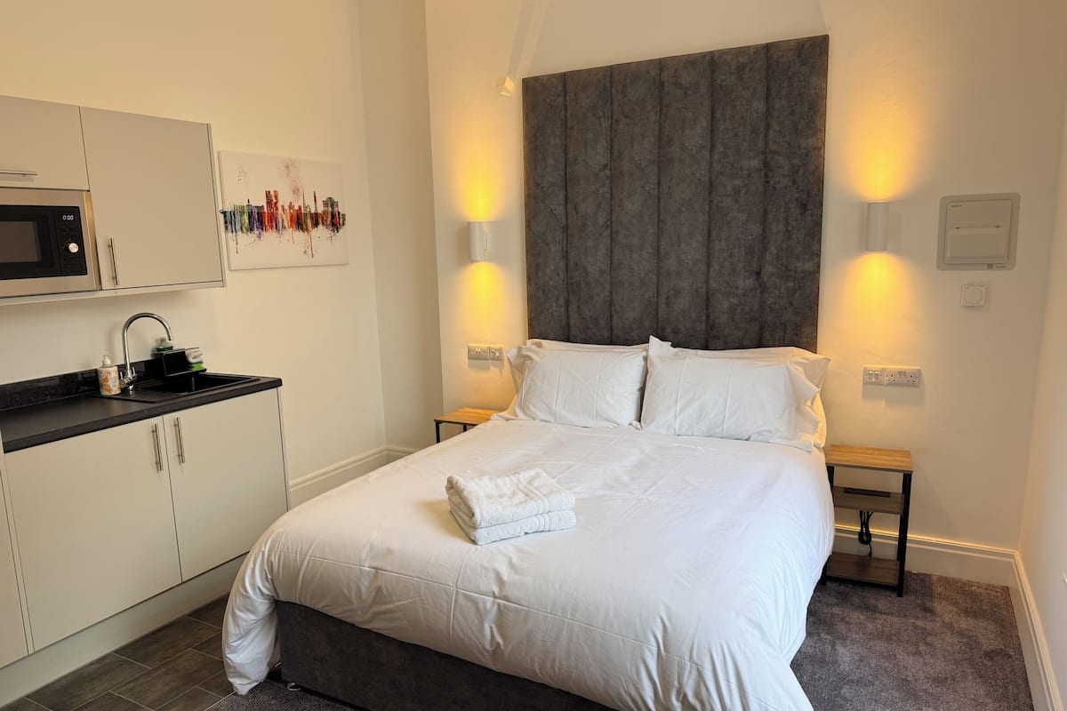 Habitación de hotel con cama, kitchenette pequeño y una obra de arte colgada en la pared.